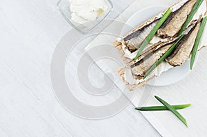 Summer light open sandwiches on crisps bread with fish preserves, feta cheese, green onion sprig on soft light white wood board.