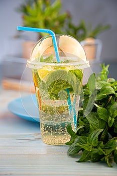 Summer mint lemon refreshing cocktail mojito with ice in plastic glass background. Carbonated mineral water. Glass for