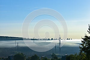 Summer misty morning. The road is in the park. Sunrise over the forest behind thick fog