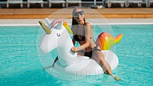 Summer mood. Beautiful girl having fun and relaxing on inflatable unicorn in pool.