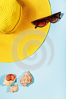 Summer mood, on a blue background lies a yellow hat, sunglasses and shells, top view