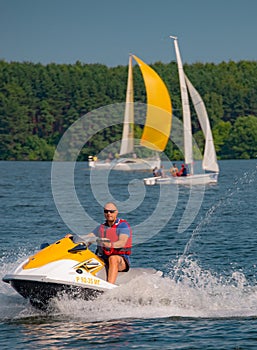 Summer mood: yellow and white sails on the blue sky background and a man on a yellow scooter .