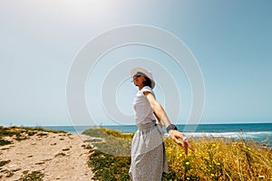 Summer mood. A young woman in a white flowing dress walks along the seashore. The girl looks at the sea