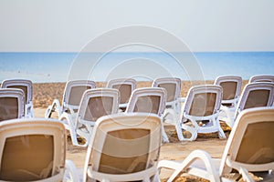 Summer morning empty sunny beach with white plastic chairs for sunbathing