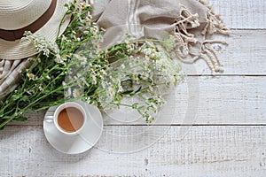 Summer morning table with a cup of coffee, wild flowers and woman`s hat