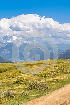 Summer mountain landscape with hiking path and snowcapped mountains in the background. Blue sky with clouds above