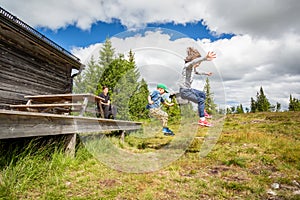 Summer nature side view of children in mid air jumping of a porch landing on grass hill.