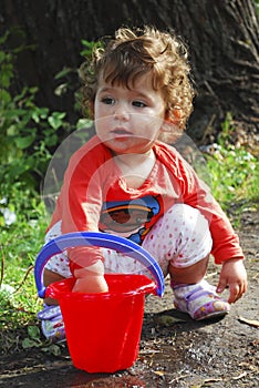 Summer near the river little girl playing with a bucket of water