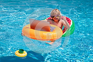 Summer office and freelance concept. Child working on laptop in summer pool. Little freelancer using computer, remote