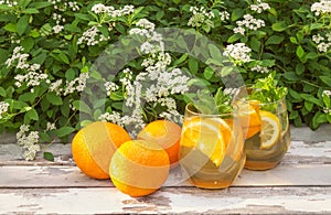 Summer orange lemonade and fresh oranges on rustic wooden table on fresh white Spiraea flowers background