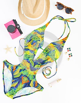 Summer outfit, beach outfit, summer stuff. Exotic pattern swimsuit, retro sunglasses, pink retro camera and straw hat. Flat lay, t