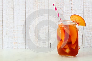 Summer peach iced tea in a mason jar glass against white wood