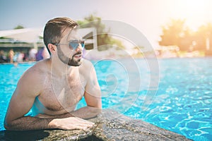 Summer photo of muscular smiling man in swimming pool. Happy male model in water on summer vacations.