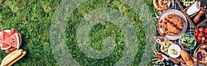 Summer picnic with cake, fruits, cheese, wine and snacks on plaid over green background. Top view. Copy space. Summer