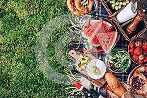 Summer picnic with cake, fruits, cheese, wine and snacks on plaid over green background. Top view. Copy space. Summer