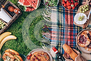 Summer picnic with cake, fruits, cheese, wine and snacks on plaid over green background. Top view. Copy space. Summer