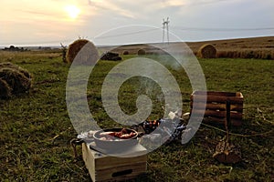 Summer picnic in the evening in the field, stacks of straw and harvested wheat. Meat is fried on fire, the fire burns down.