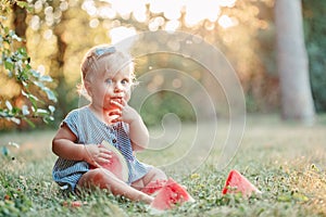 Summer picnic food. Cute Caucasian baby girl eating ripe red watermelon in park. Funny child kid sitting on ground with fresh