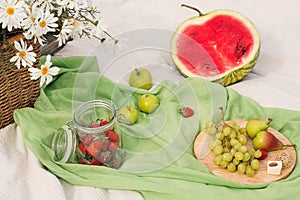 Summer picnic in the meadow on the green grass. Fruit basket, juice and bottled wine, watermelon, strawberries in a