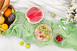 Summer picnic in the meadow on the green grass. Fruit basket, juice and bottled wine, watermelon, strawberries in a