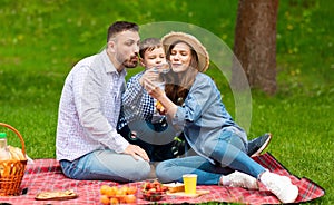 Summer picnic in park. Millennial parents with their cute son having fun with soap bubbles outside