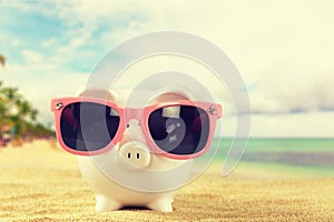 Summer piggy bank with sunglasses on the beach