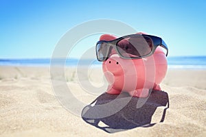 Summer piggy bank with sunglasses on the beach