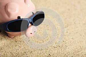 Summer piggy bank with sunglasses standing on the beach