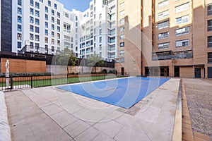 A summer pool covered with canvas to spend the winter in the common areas of an urbanization with gardens, trees and terrazzo