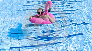 Summer pool relaxing. Young sexy woman in bikini swimsuit, sunglasses float with pink flamingo in blue water. Trendy summer