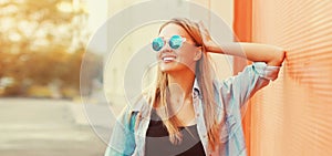 Summer portrait of beautiful blonde smiling young woman wearing sunglasses in the city