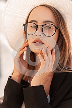 Summer portrait beautiful fashionable young woman in fashion glasses in straw white hat in youth black stylish jacket at sunset.