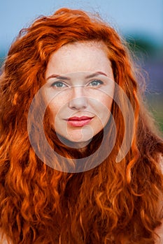 Summer portrait of a beautiful girl with long curly red hair