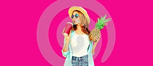 Summer portrait of beautiful woman drinking juice and holding pineapple wearing straw hat, sunglasses on pink background