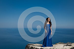 Summer portrait. Beautiful woman standing on a cliff over blue s