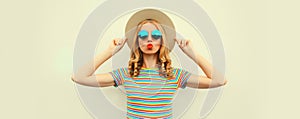 Summer portrait of beautiful young woman blowing her lips sending sweet air kiss wearing straw round hat on white background