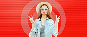 Summer portrait of beautiful young woman blowing her lips sends air kiss wearing summer straw hat, denim jacket and backpack on