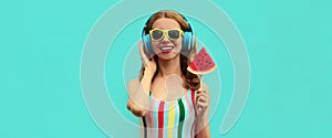Summer portrait cheerful happy smiling young woman in headphones listening to music with juicy slice of watermelon on a blue