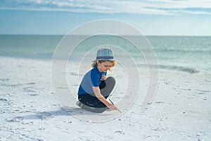 Summer portrait of childen draws on the sand. Boy drawing on sand at seaside. Child drawing sand by imaginary on beach