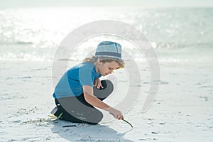 Summer portrait of childen draws on the sand. Boy drawing on sand at seaside. Child drawing sand by imaginary on beach