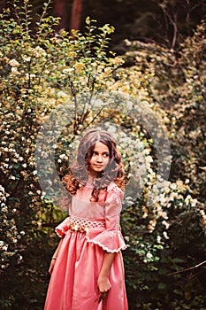 Summer portrait of curly smiling child girl in pink fairytale princess dress in the forest