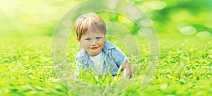 Summer portrait of cute smiling child playing lying on the grass in the park on a sunny day on blurred background