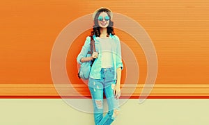 Summer portrait of full-length happy smiling young woman wearing straw hat, backpack and shirt on orange background