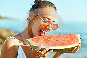 Summer portrait funny girl in red glasses holding huge slice of watermelon and bites him with pleasure.