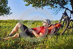 Summer portrait of handsome young man lying on green meadow near bike and backpack.