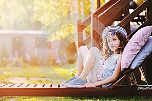 Summer portrait of happy kid girl relaxing on lounger in garden