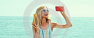 Summer portrait of happy laughing young woman taking selfie with smartphone with papaya on the beach on sea background