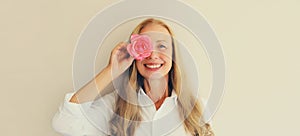 Summer portrait of happy smiling middle aged woman covering her eyes with pink rose flower buds