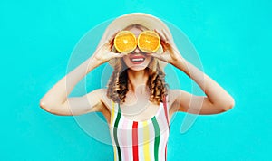 Summer portrait happy smiling woman holding in her hands two slices of orange fruit hiding her eyes in straw hat on colorful blue