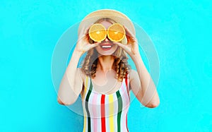 Summer portrait happy smiling woman holding in her hands two slices of orange fruit hiding her eyes in straw hat on colorful blue